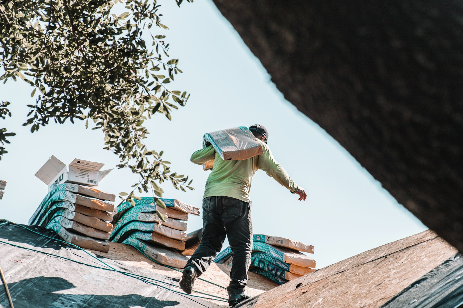 Roofer carrying shingle bundles across a new roof deck during a replacement